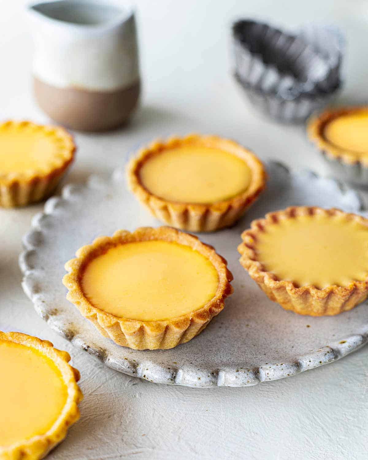 3 golden egg tarts on a plate, surrounded by 3 more off the plate.