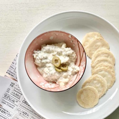 A bowl of olive and cream cheese dip with crackers around it.