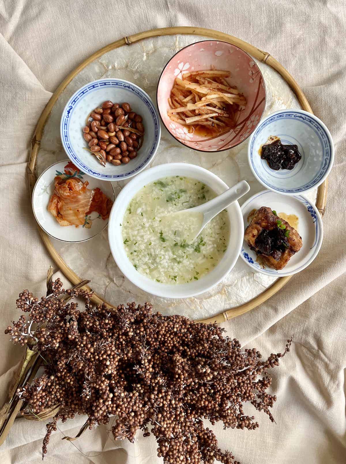 A bowl of chicken rice porridge with various vegetable side dishes.