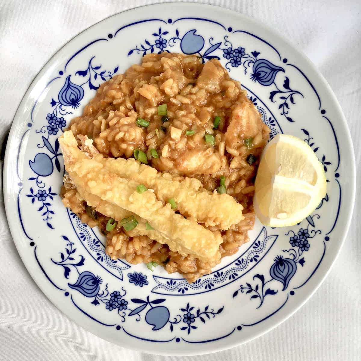 A plate of seafood risotto with fried Japanese tempura on top.