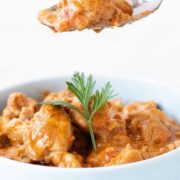 Butter chicken being scooped out of a white bowl.