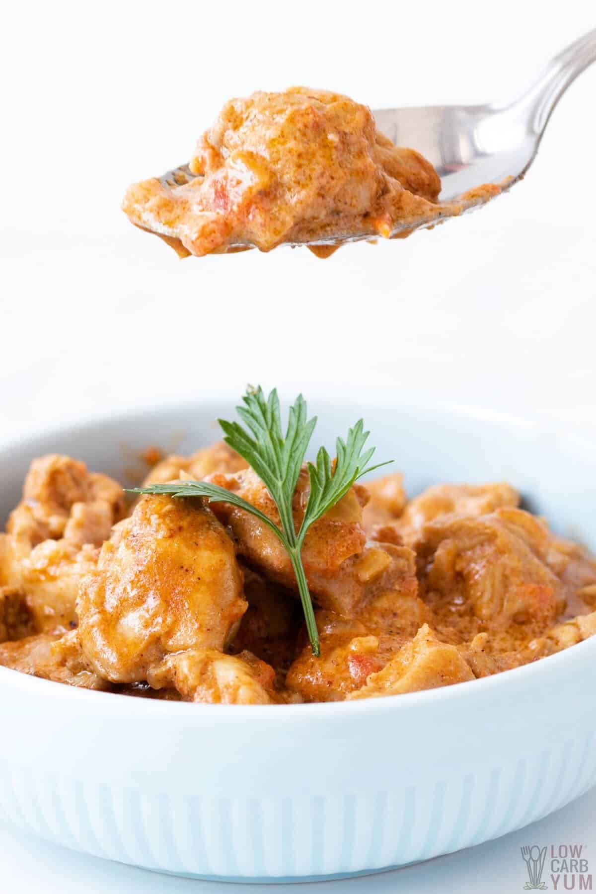 Butter chicken being scooped out of a white bowl.