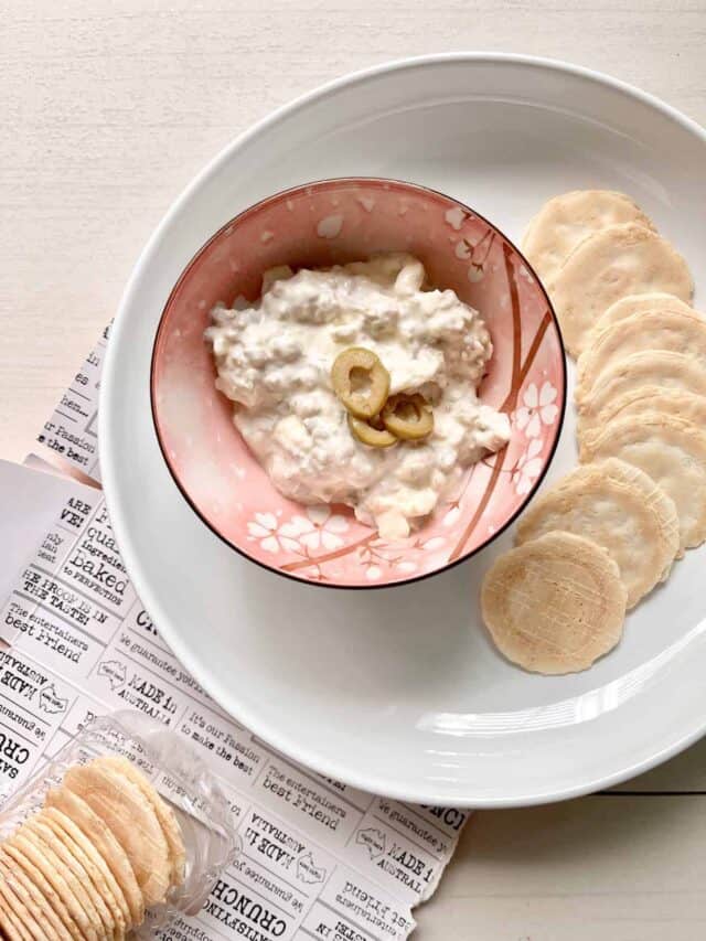 A bowl of olive mayonnaise and cream cheese dip with crackers around it.