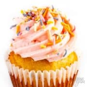 Close-up of a vanilla cupcake with raspberry frosting and sprinkles.