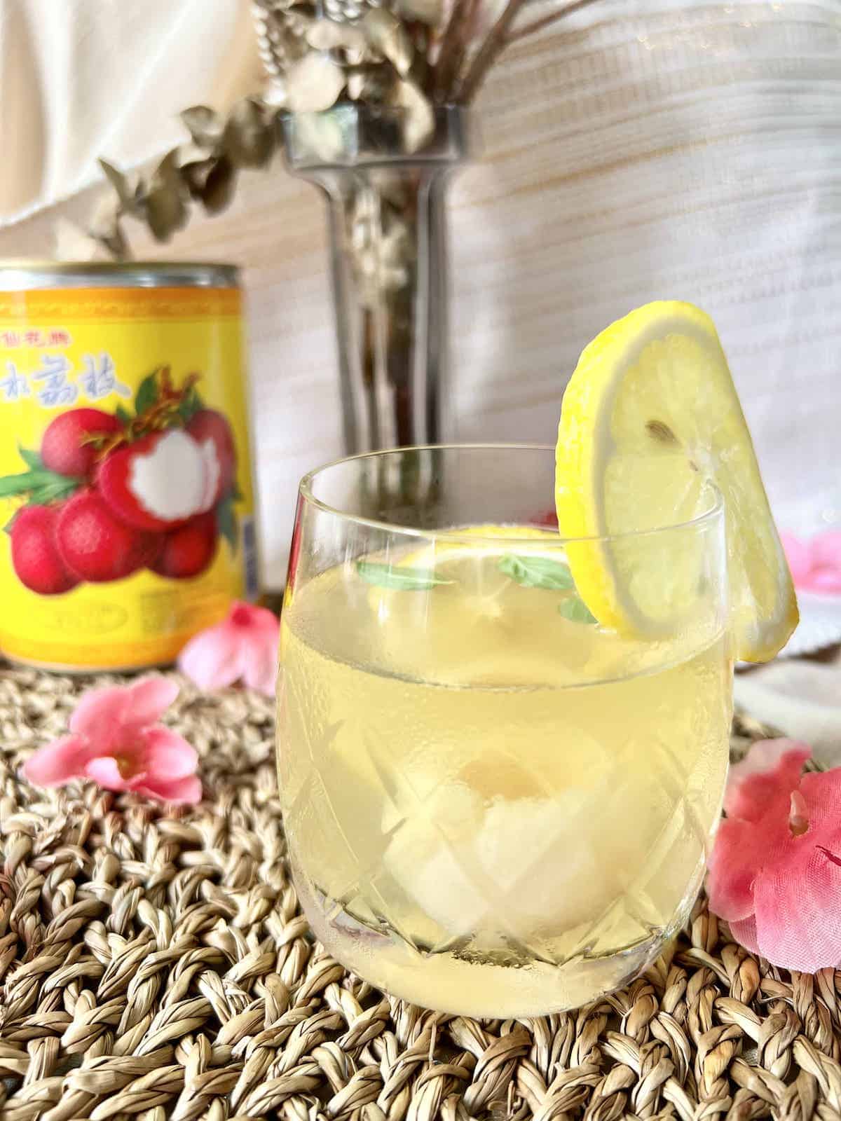 A glass of iced lychee tea with a can of lychees behind it.