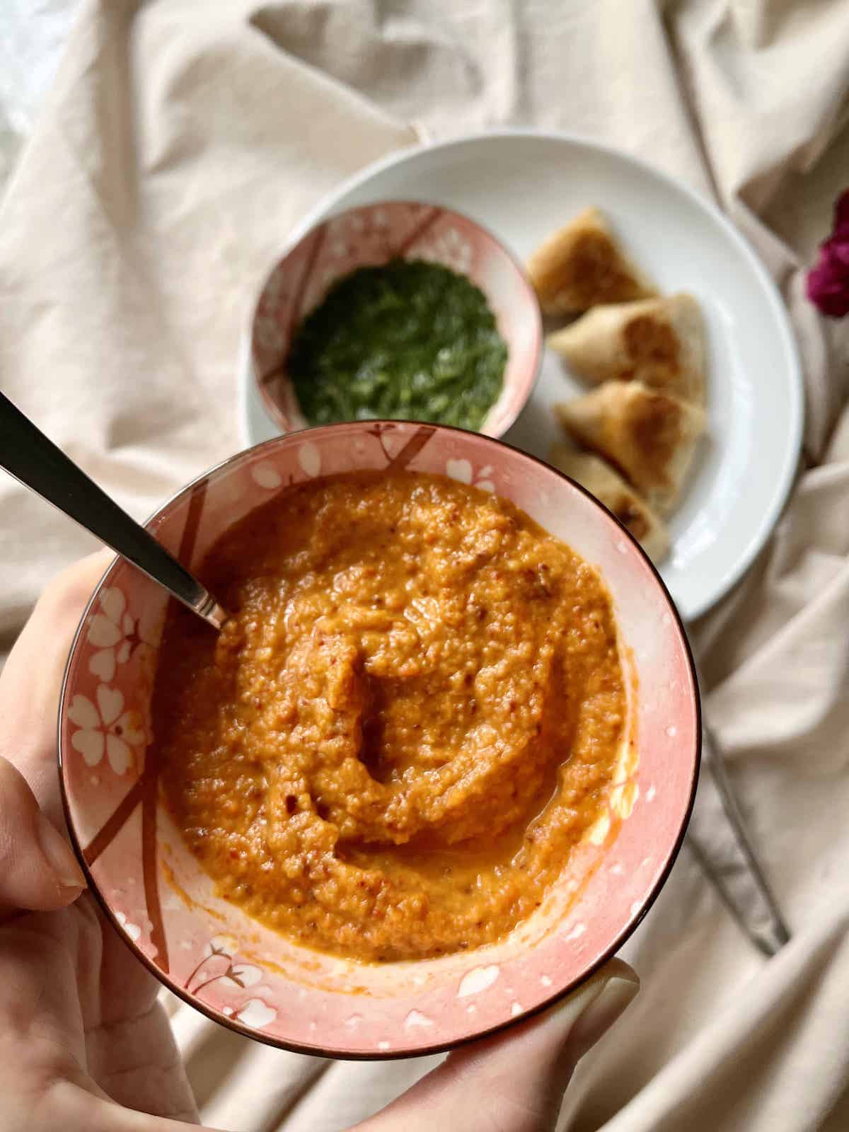 Close-up of a red samosa dipping sauce with samosas and green sauce in the background.,