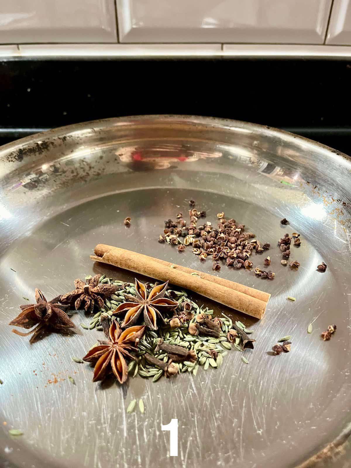Whole spices being dry fried in a stainless steel pan.
