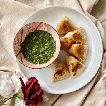 Little samosas with tomato chutney and a bowl of green cilantro dipping sauce.