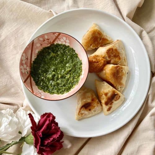 Little samosas with tomato chutney and a bowl of green cilantro dipping sauce.