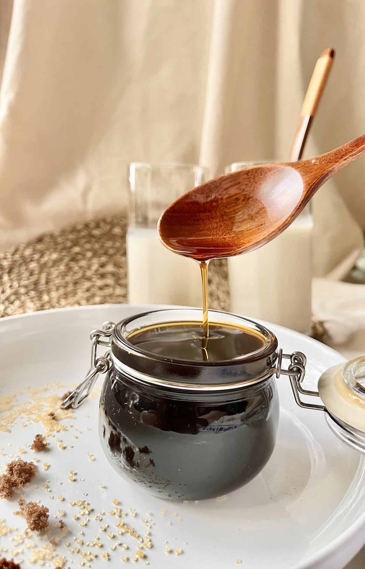 A photo of a thinner brown sugar sauce flowing quickly off a wooden spoon.