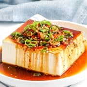 A close-up of a Korean tofu side dish glistening with a soy sauce dressing.