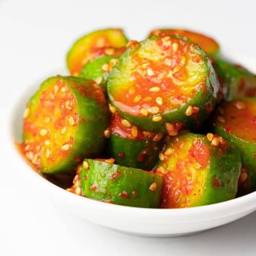 Close-up of cut cucumbers drizzled with a spicy Korean sauce.