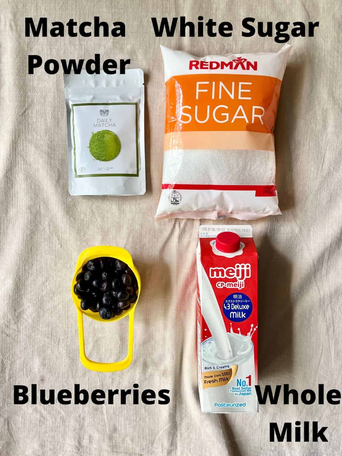 The 4 ingredients for blueberry matcha latte laid out on a linen tablecloth and labelled.