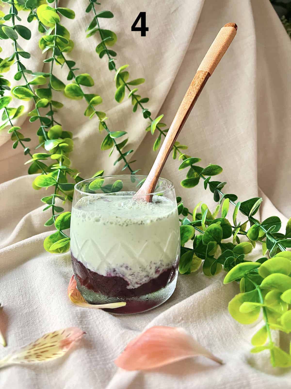 Matcha milk poured over blueberry puree in a glass cup.