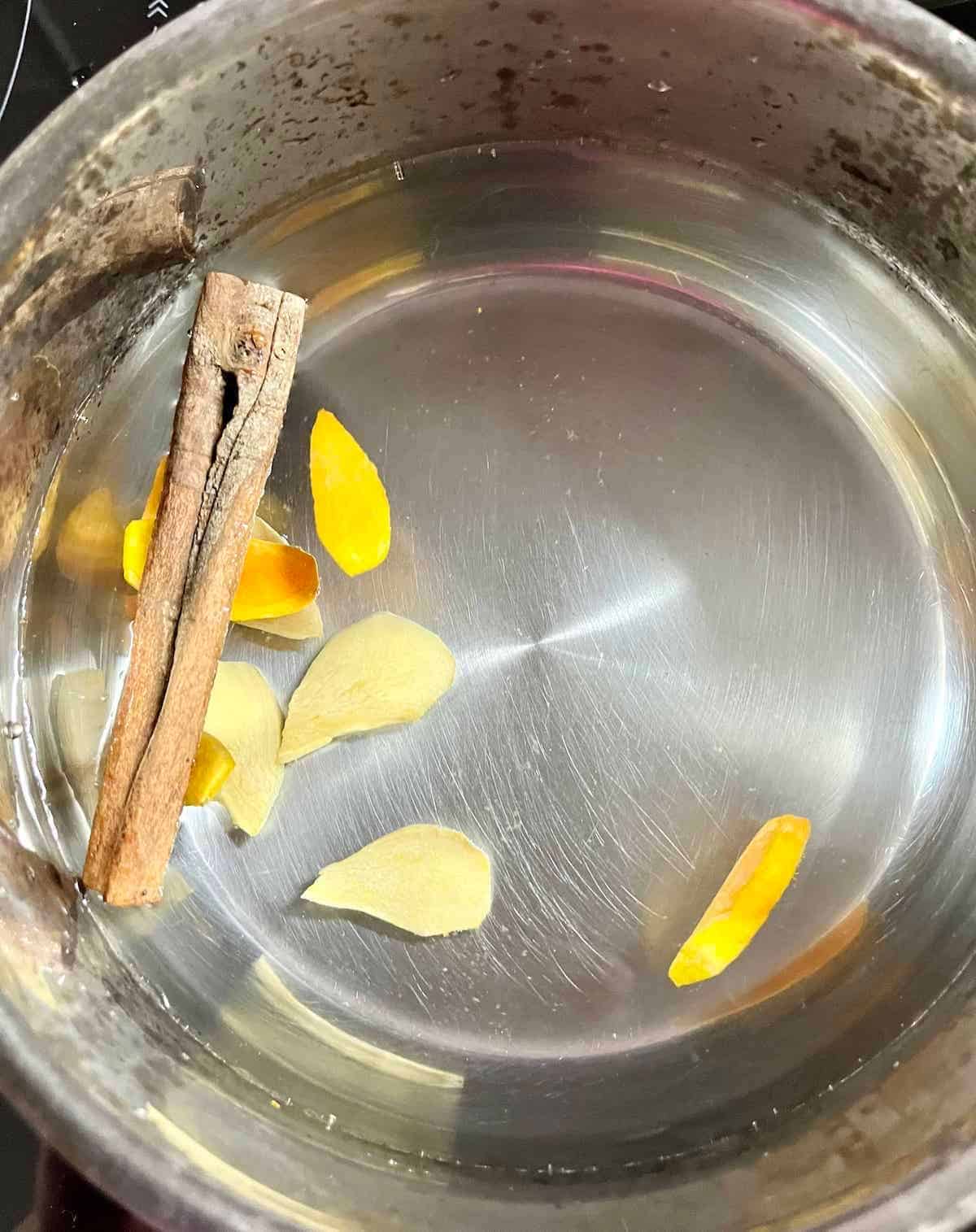 Boiling slices of ginger and turmeric with cinnamon in a pot.