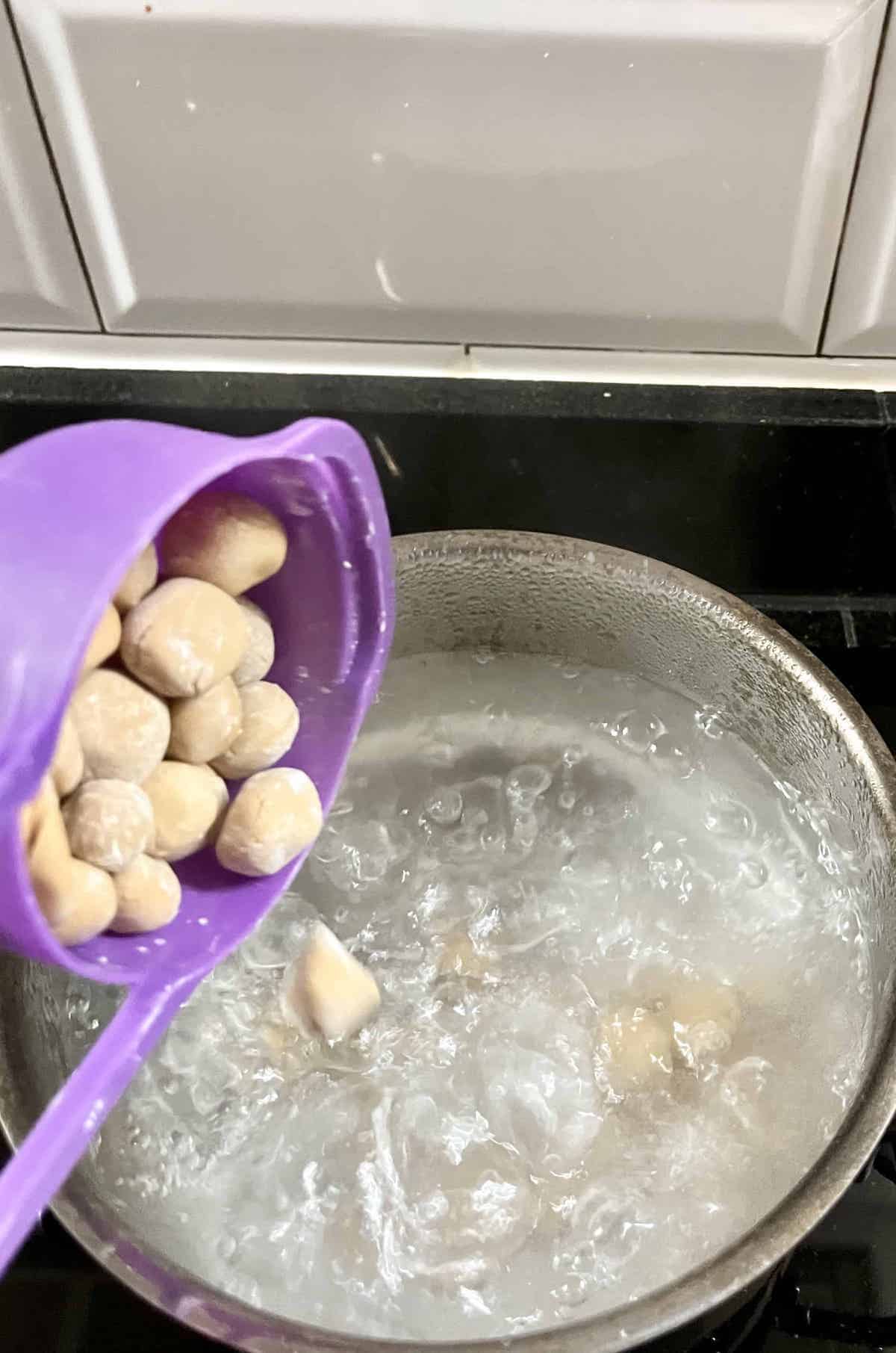 Brown sugar pearls being added to a pot of boiling water.