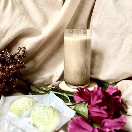 A glass of cold Hojicha tea latte next to pandan cookies and flowers.