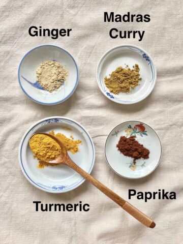 A saucer of dried ginger powder, dried madras curry powder, paprika and turmeric powder.