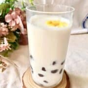 A glass of cold jasmine bubble tea with tapioca pearls and an edible flower.