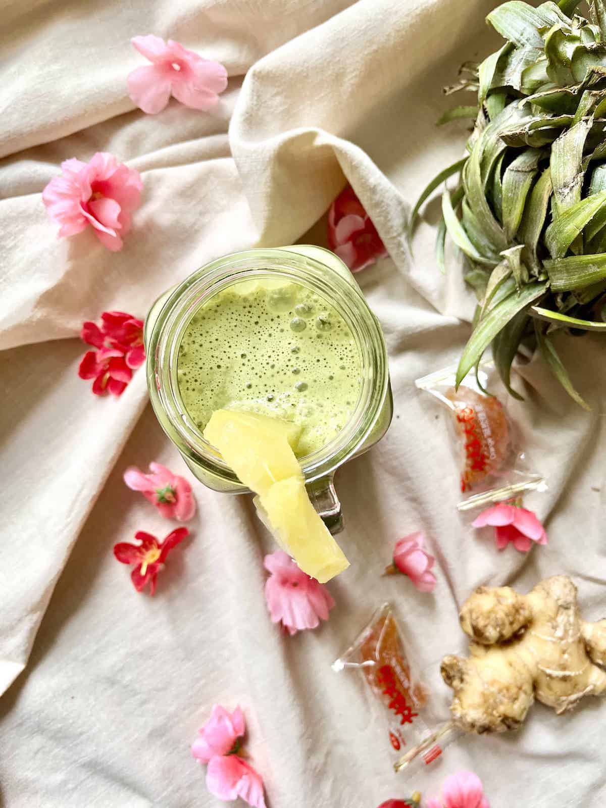 A glass of green matcha, pineapple and ginger coconut juice amongst pink flowers.