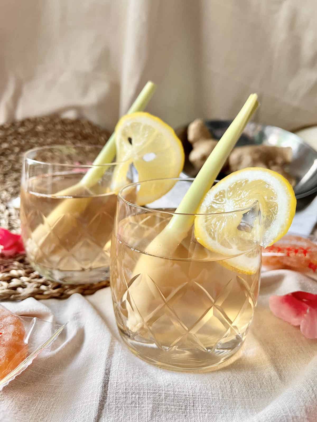 2 glasses of tea with lemongrass sticks and a slice of lemon on them.