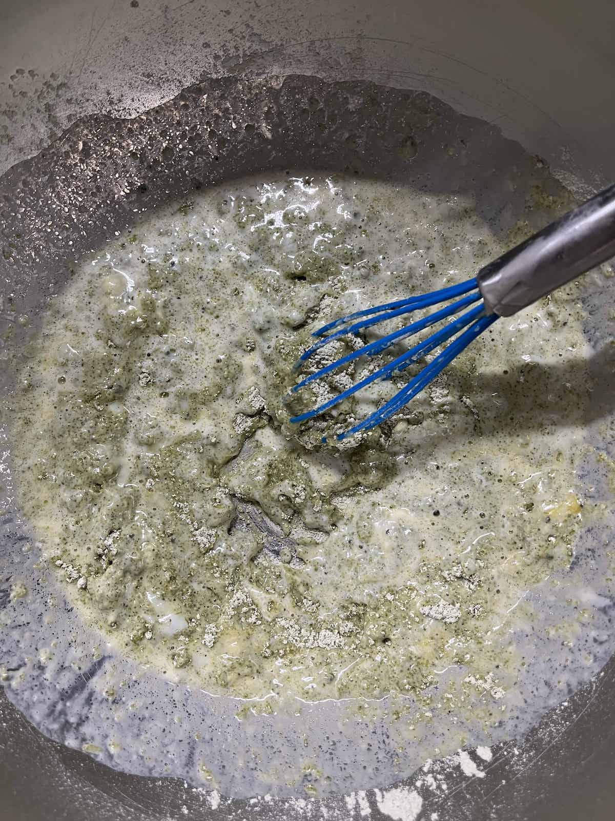 Whisking a wet batter in a stainless steel bowl.