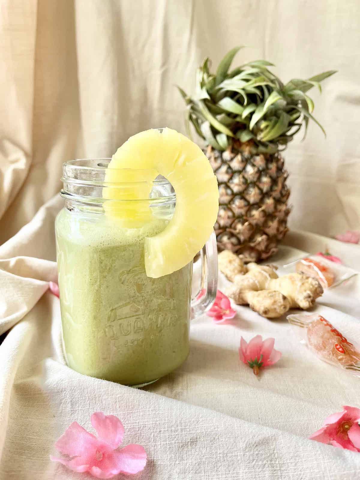 A glass mug full of green pineapple, matcha, ginger and coconut shake with a pineapple behind.