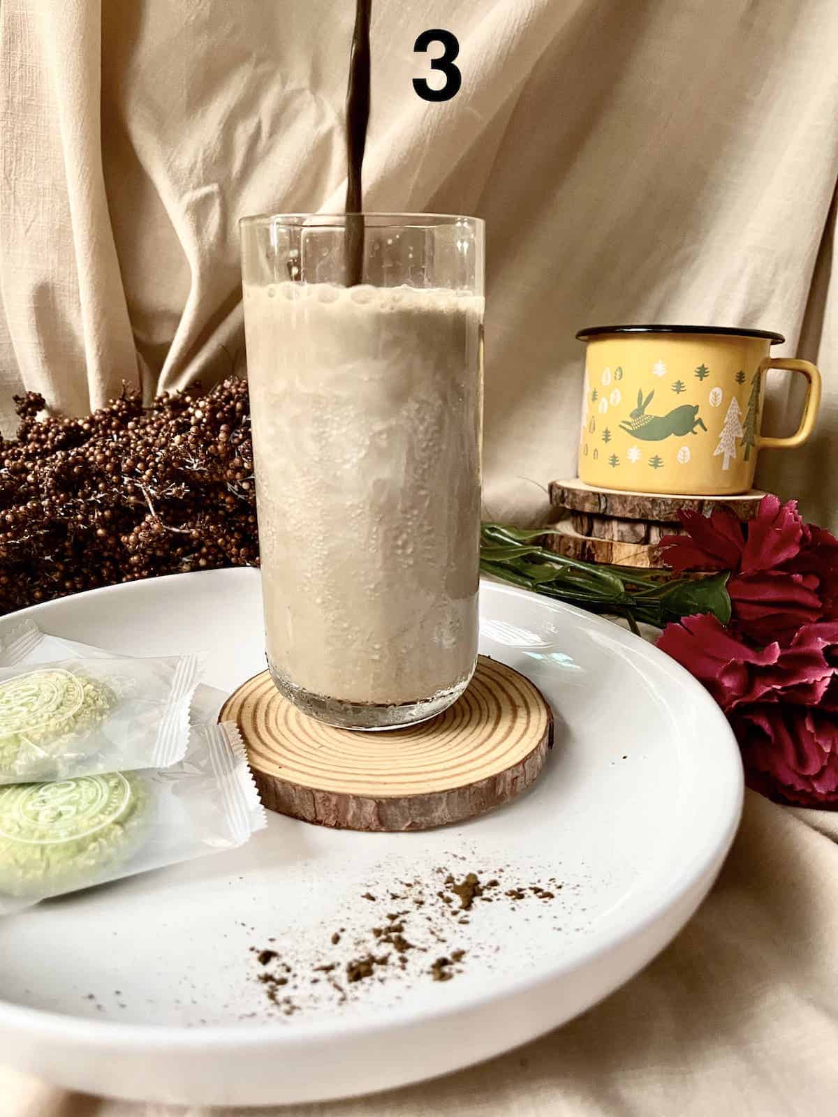 Pouring strong Hojicha tea into a glass of milk to make a latte.