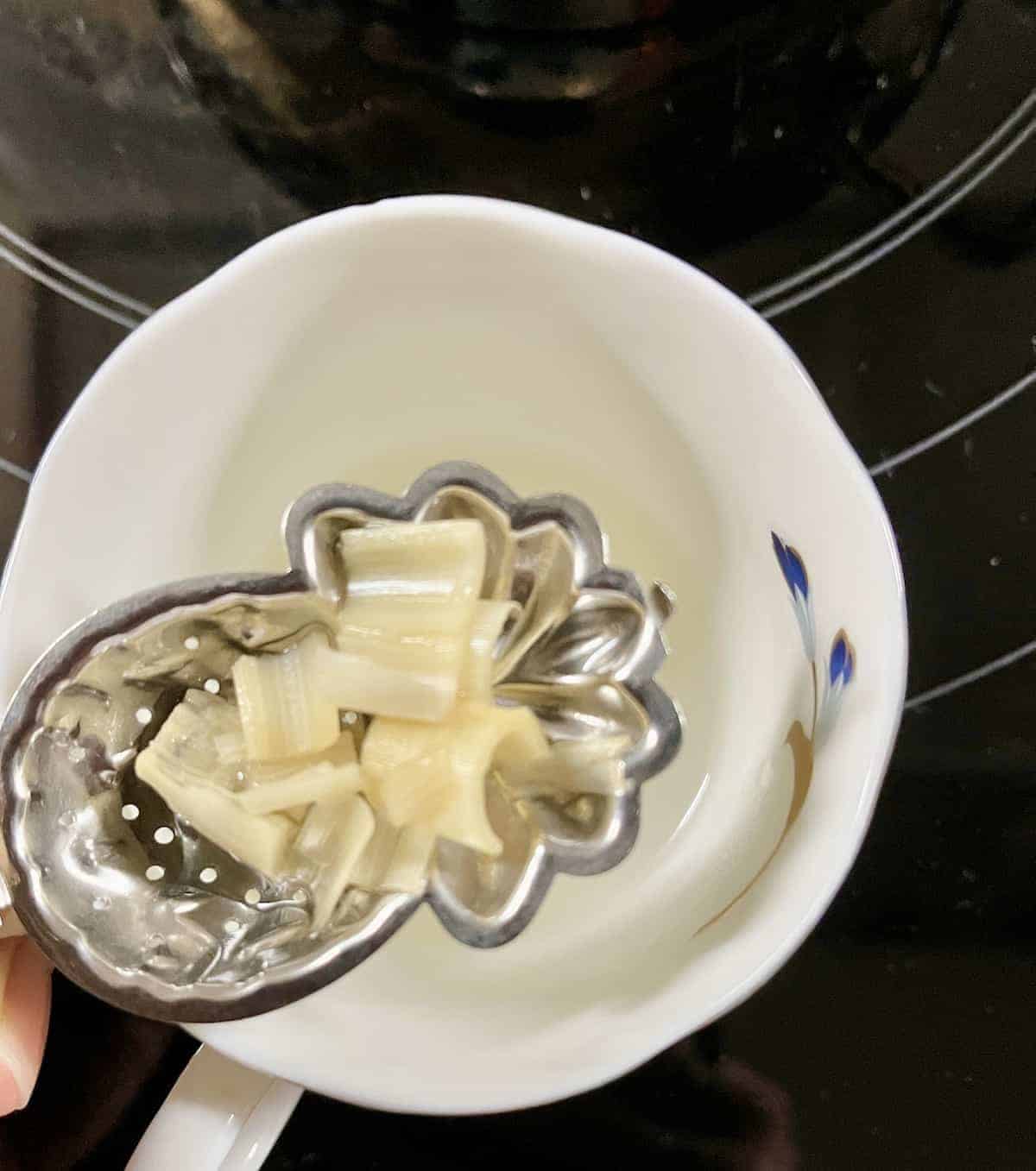 Sieving the lemongrass and ginger out before pouring lemongrass tea into a cup.