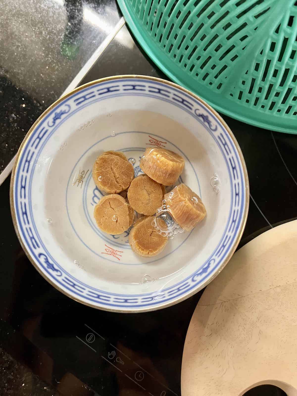 6 dried scallops soaking in a bowl of water.