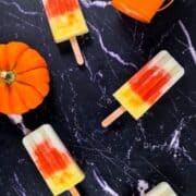 4 colourful fruit popsicles on a black surface.