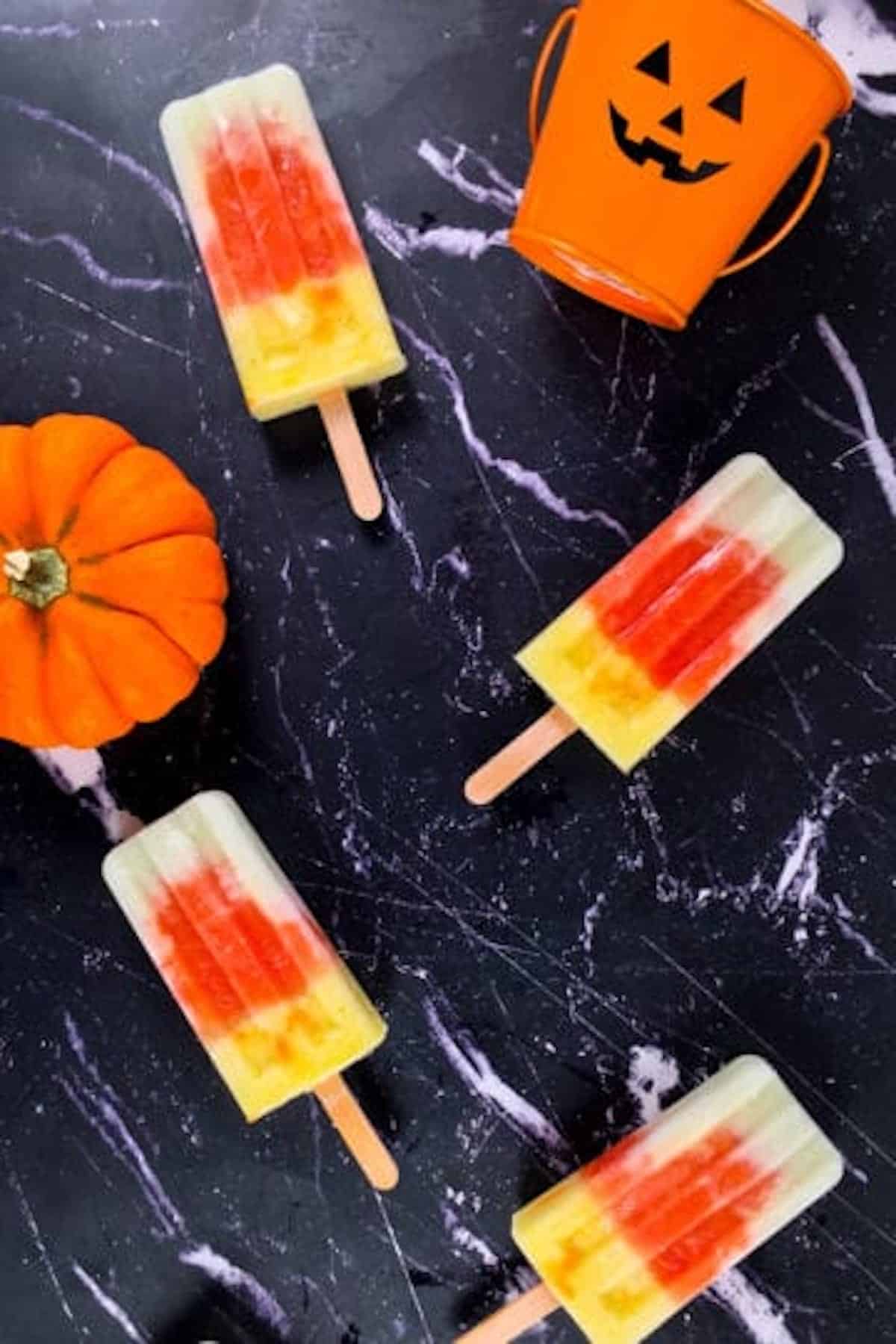 4 colourful fruit popsicles on a black surface.