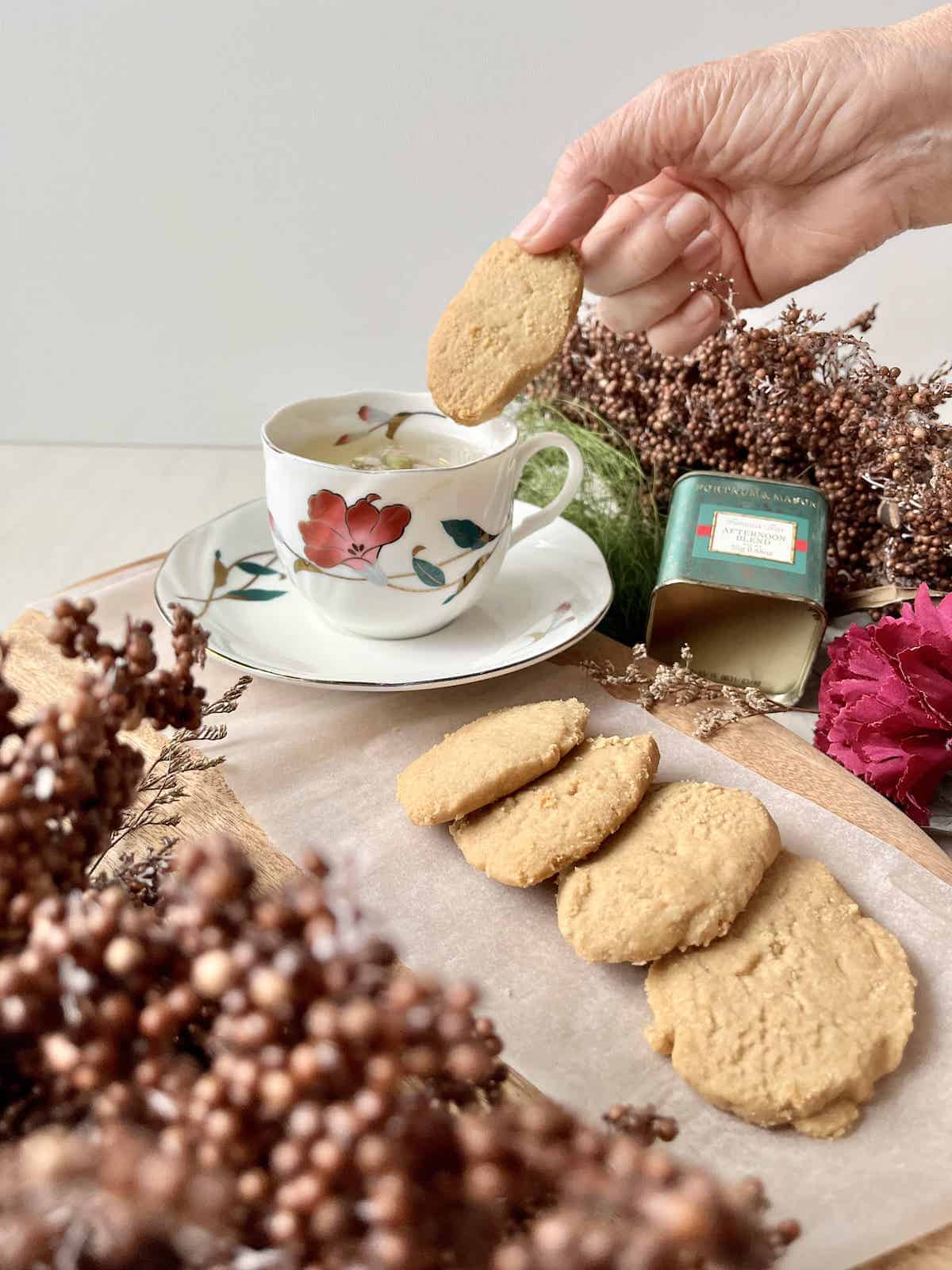 A hand dipping a brown sugar cookie into a cup of afternoon tea.