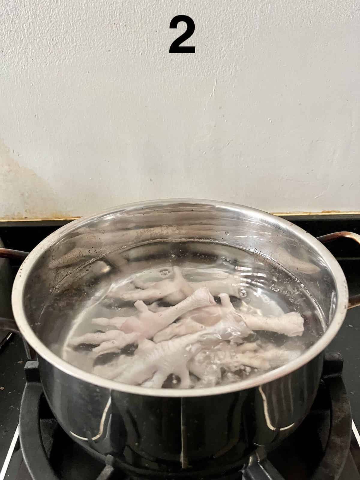 A pot of chicken feet being blanched in cold water.