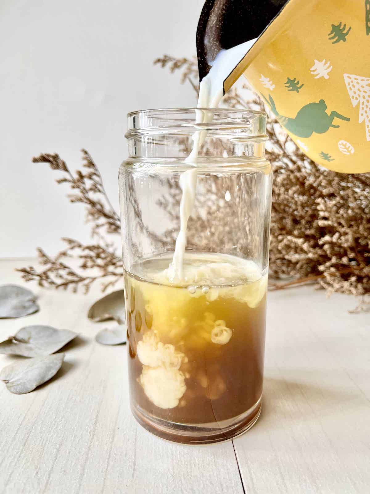 Pouring frothed milk into a cup of green tea and chai syrup.