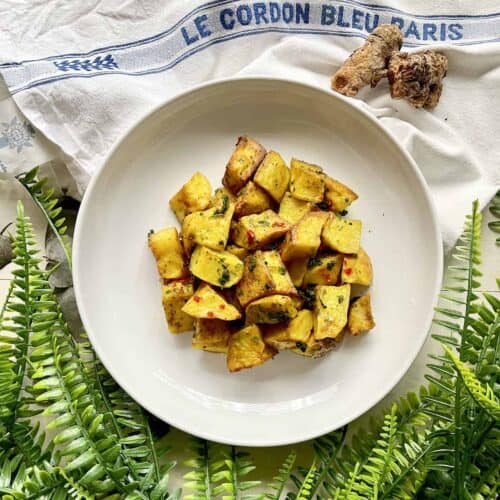 Roasted potatoes which are beautifully golden thanks to turmeric on a white plate.