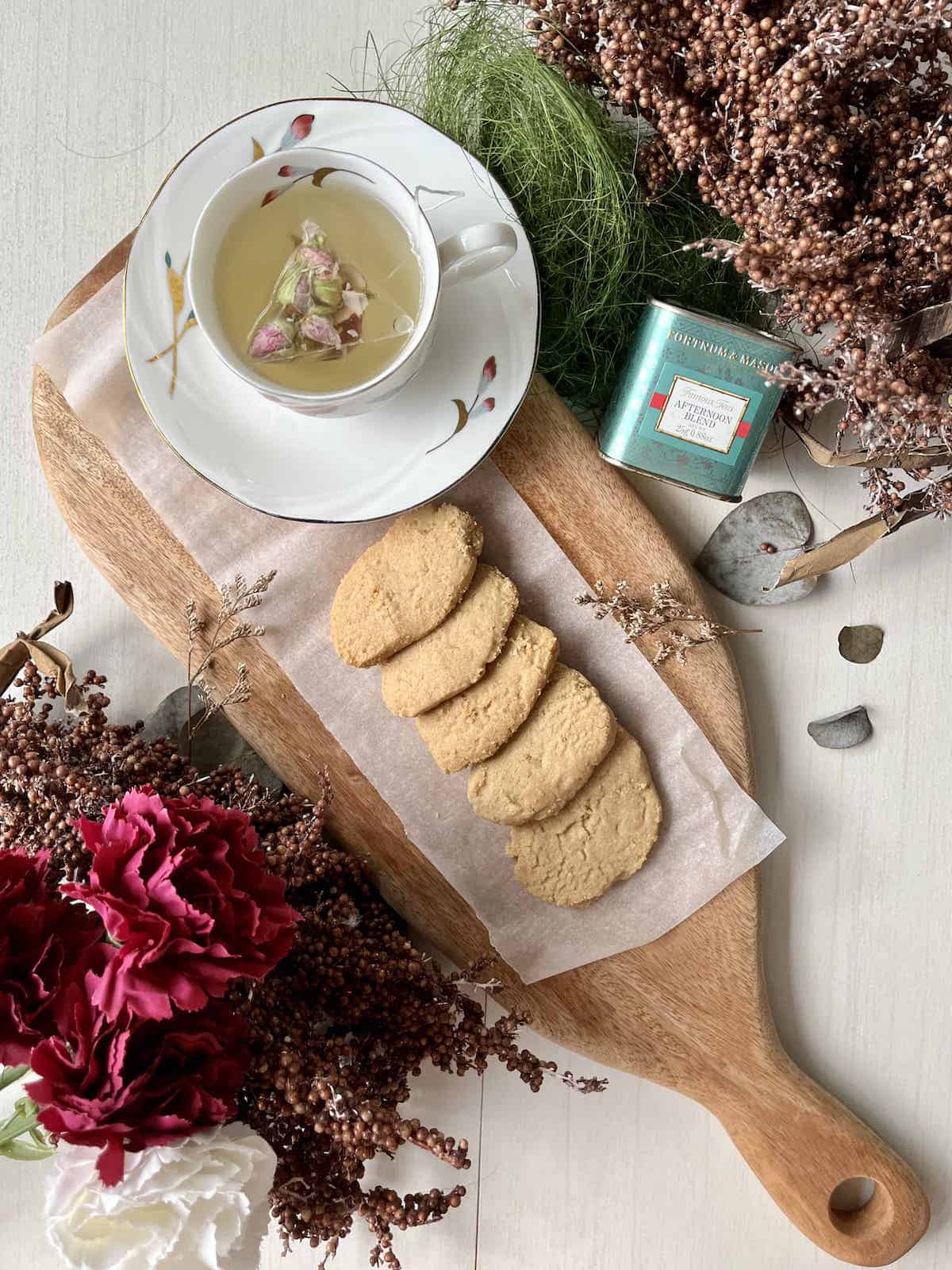 A row of homemade brown sugar butter cookies next to a cup of rose tea.