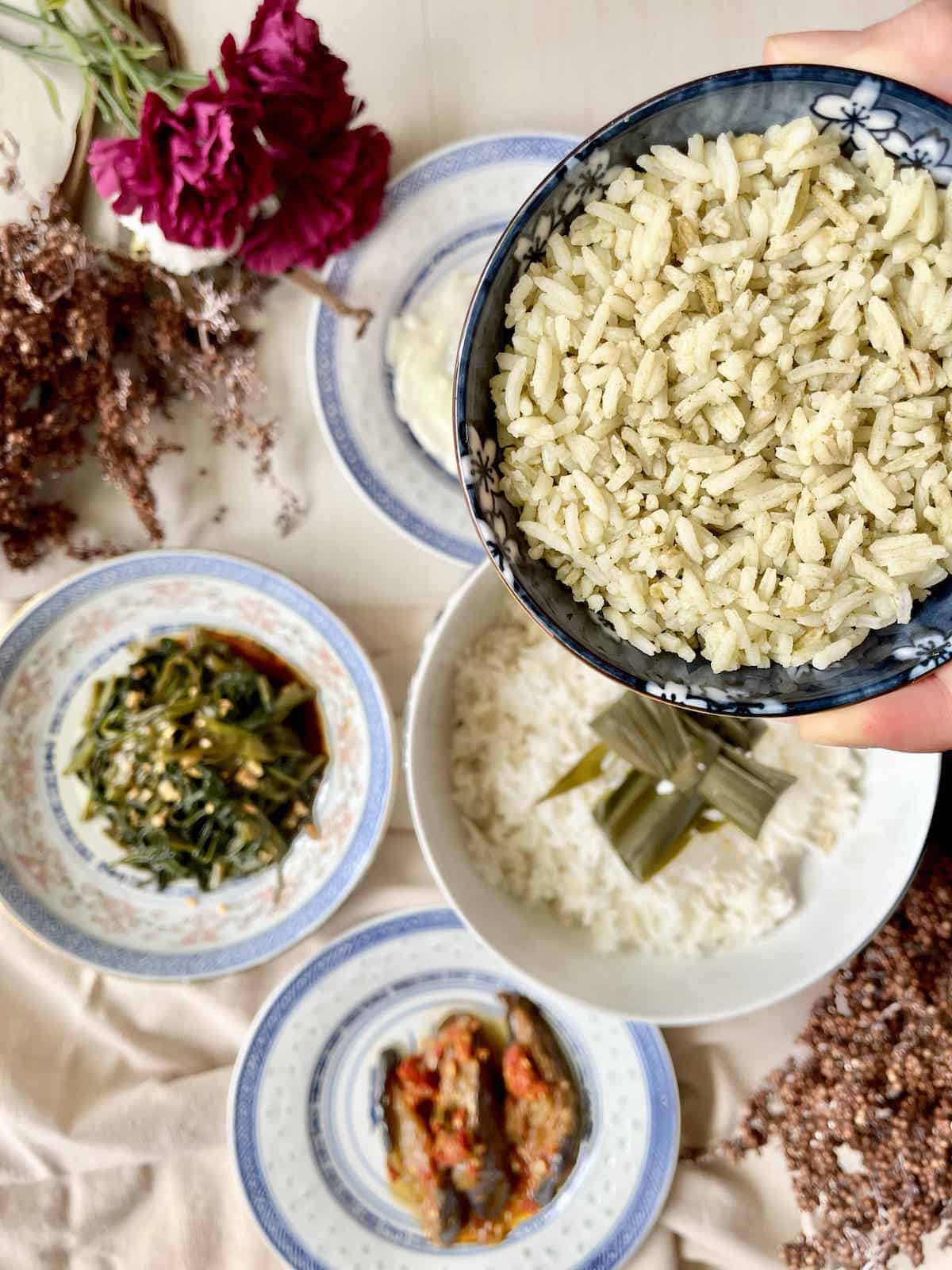 Close-up of a bowl of green pandan juice rice with Asian dishes in the background.