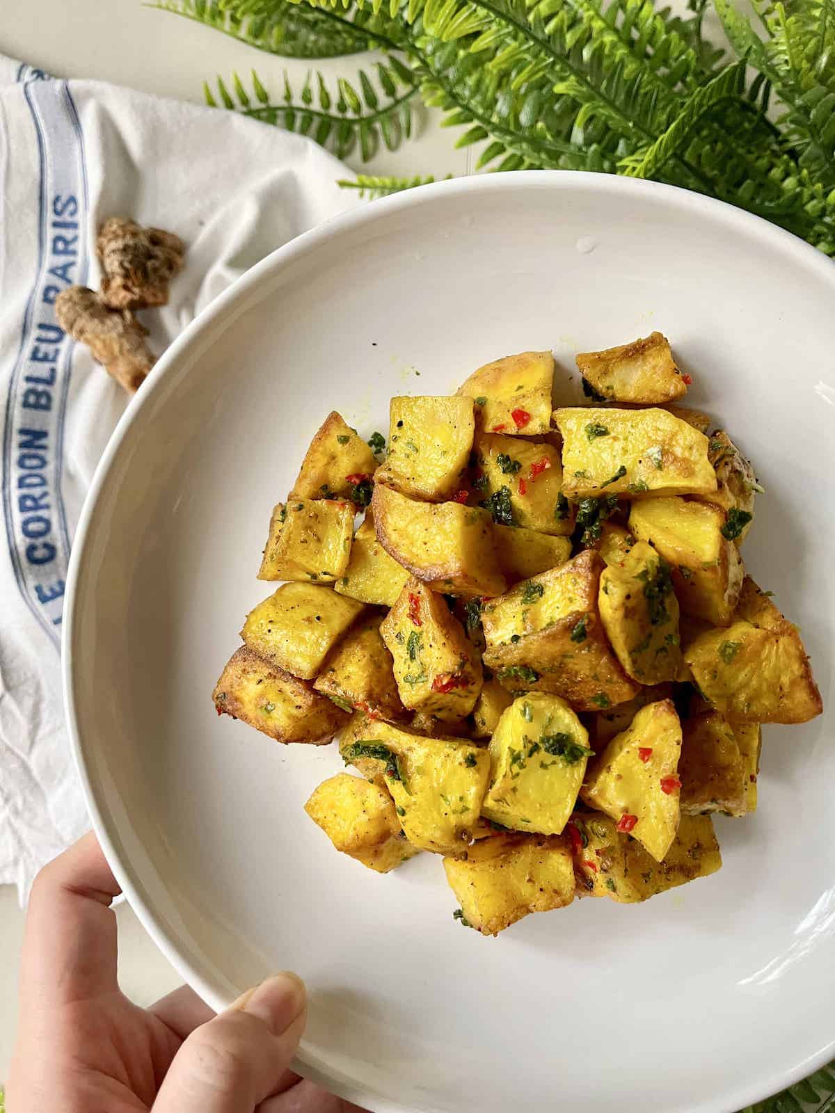 A close-up of baked turmeric potatoes on a white plate.