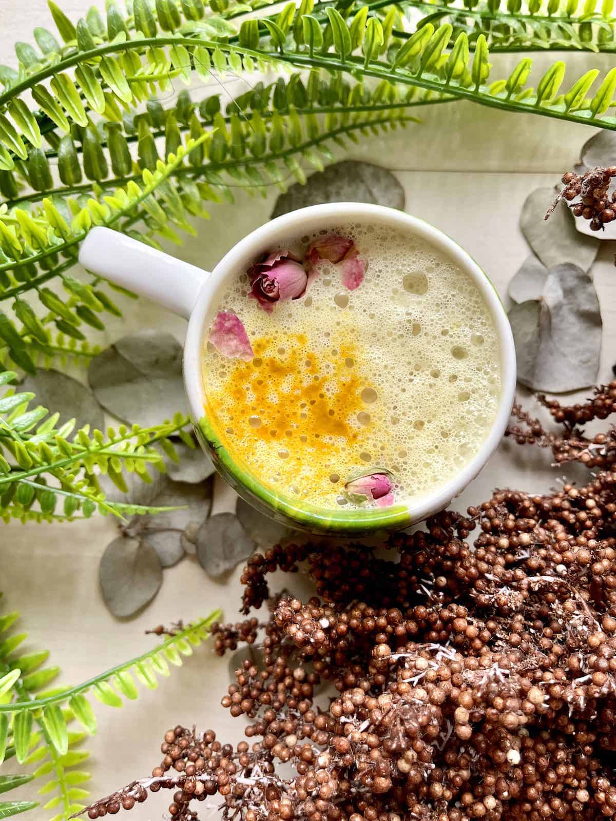 A cup of Golden Turmeric Chai Latte with Rosesbuds on a foamy top.