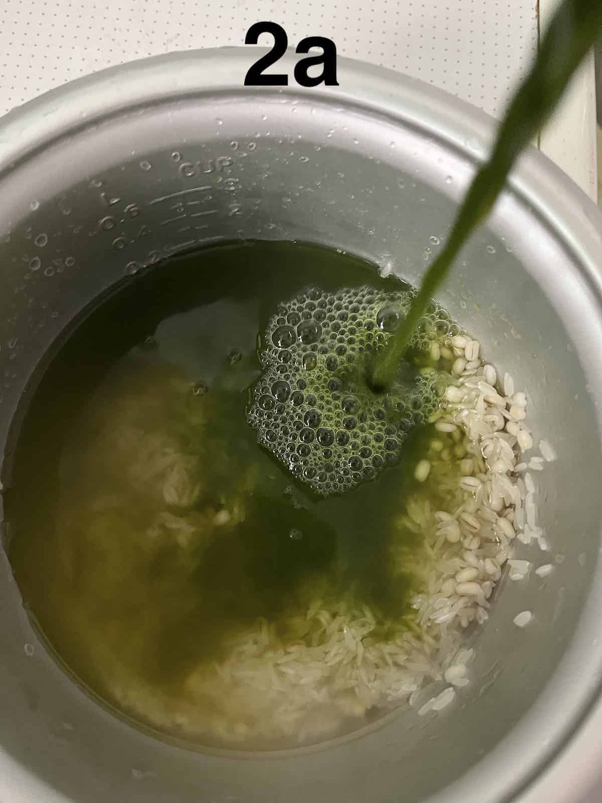 Pouring grassy green homemade pandan juice into the rice cooker.