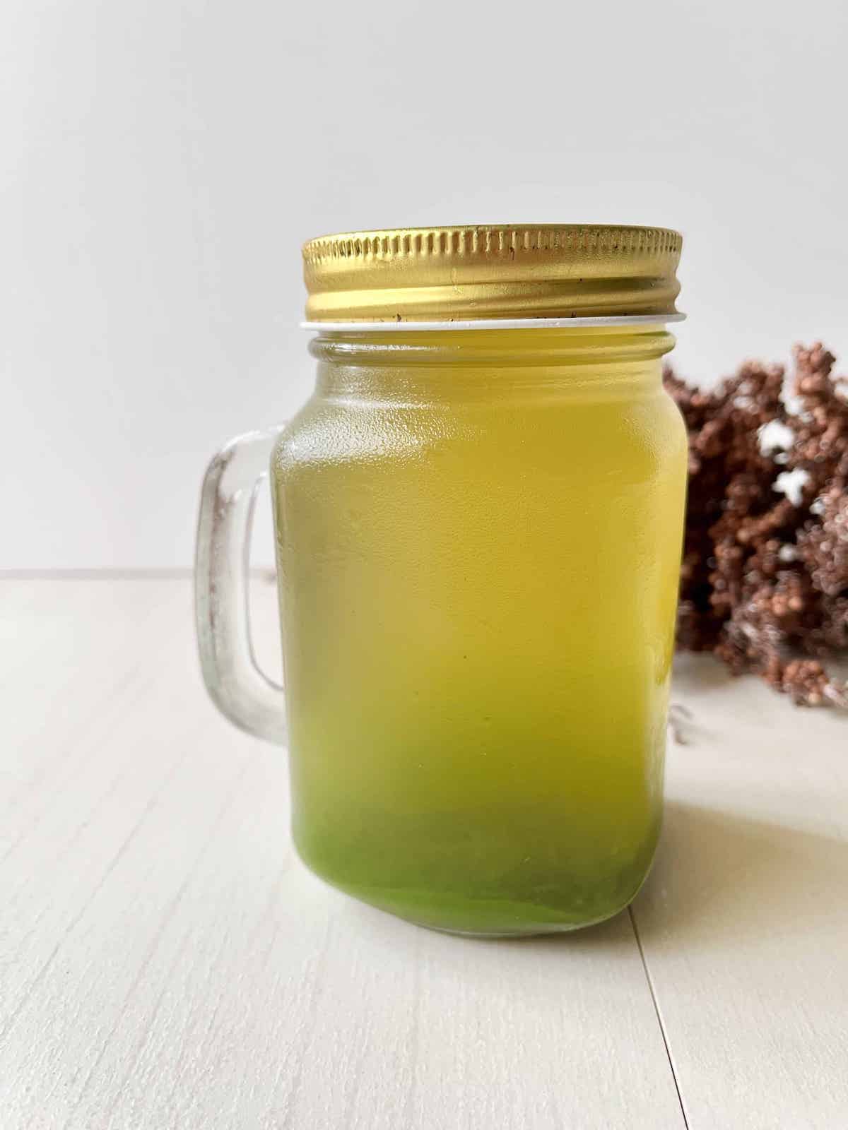 A container of pandan juice that has had the darker pandan extract settle at the bottom.