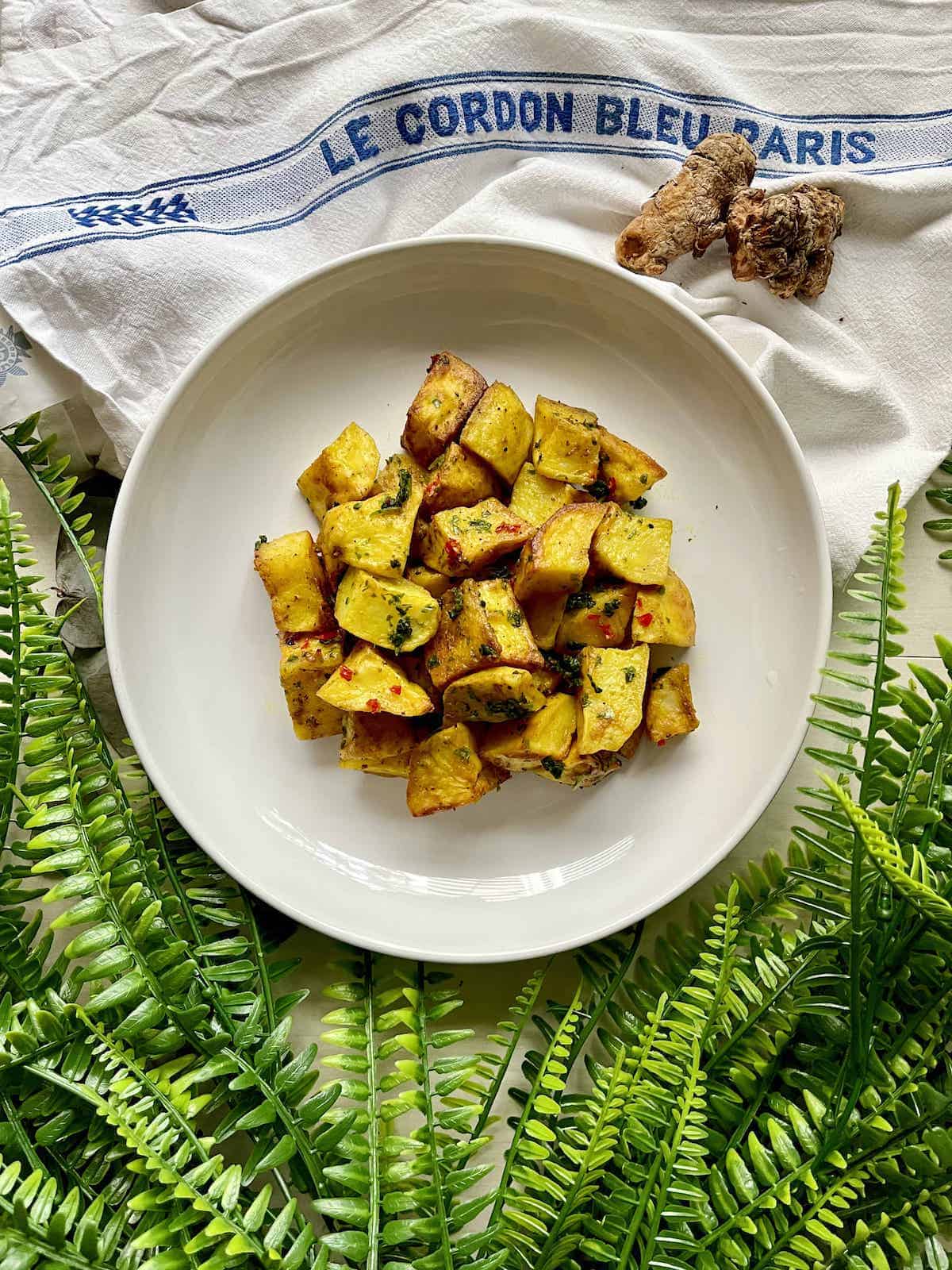 A plate of spiced potatoes next to fresh turmeric root.