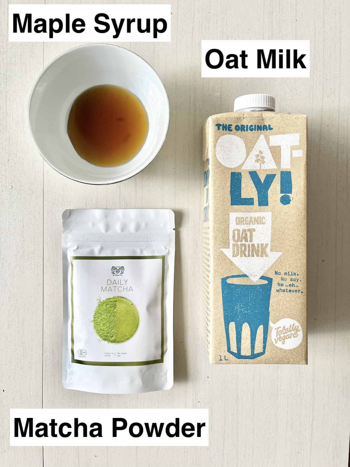 A carton of oat milk, a bowl of maple syrup and a packet of matcha powder.