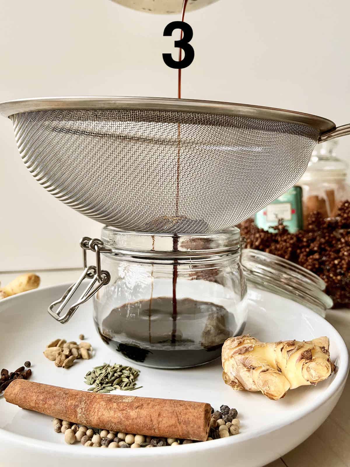 Pouring the Chai Syrup through a sieve to strain out the whole spices.