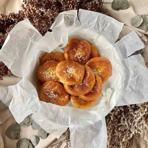 Many fried orange pancakes with sesame seeds in a bowl on baking paper.