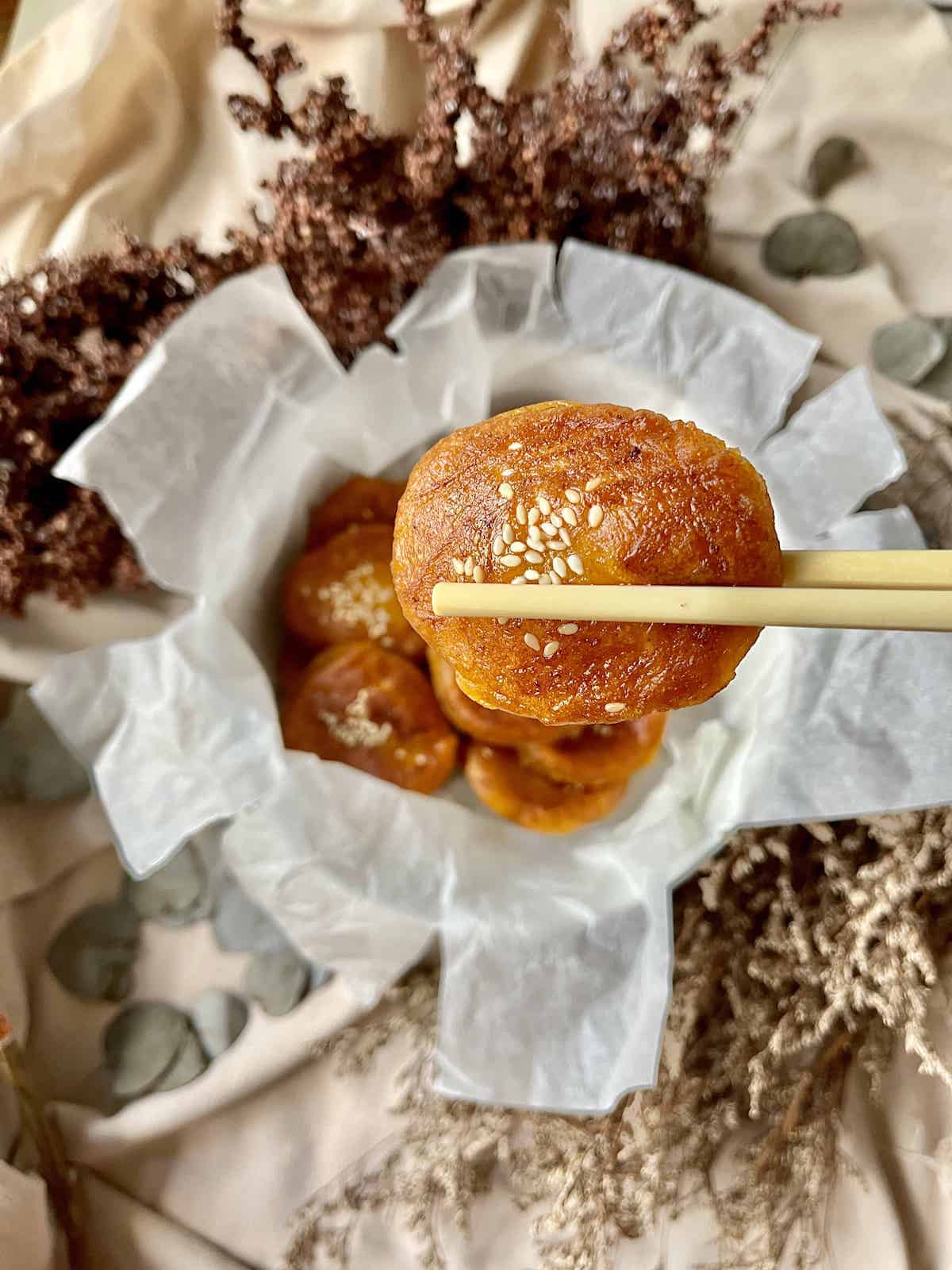 A pair of chopsticks picking up a very soft orange glutinous rice cake.