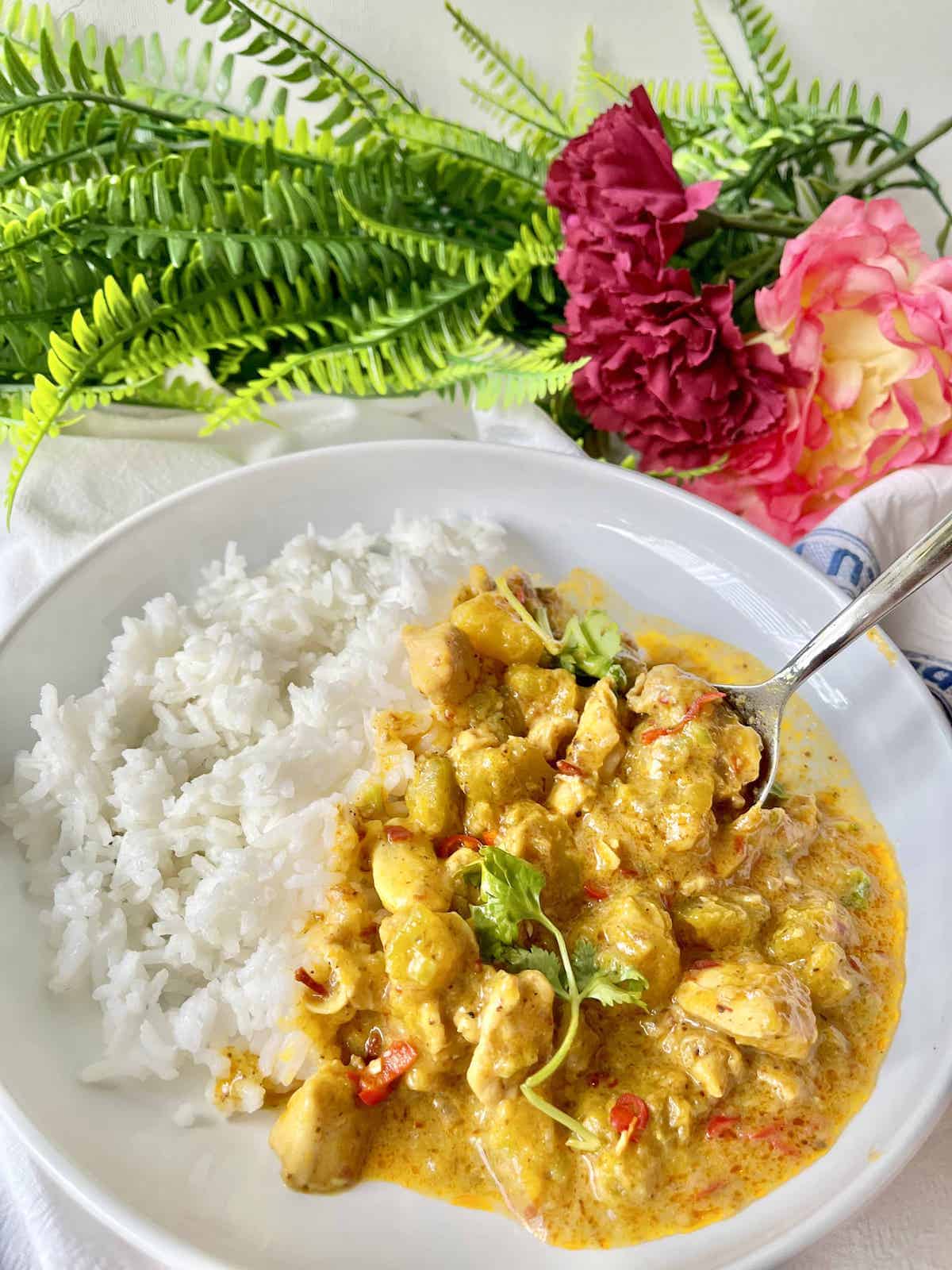 Someone scooping up thick pumpkin chicken curry with white rice.