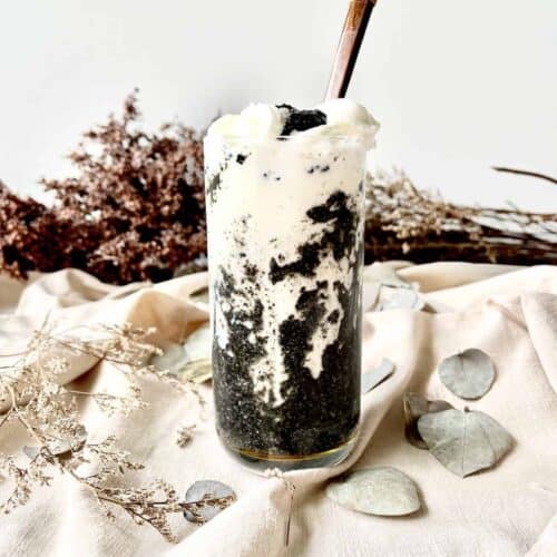 A glass of black and white black sesame latte with whipped cream on top.