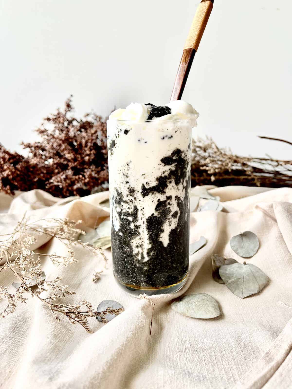 A glass of black and white black sesame latte with whipped cream on top.